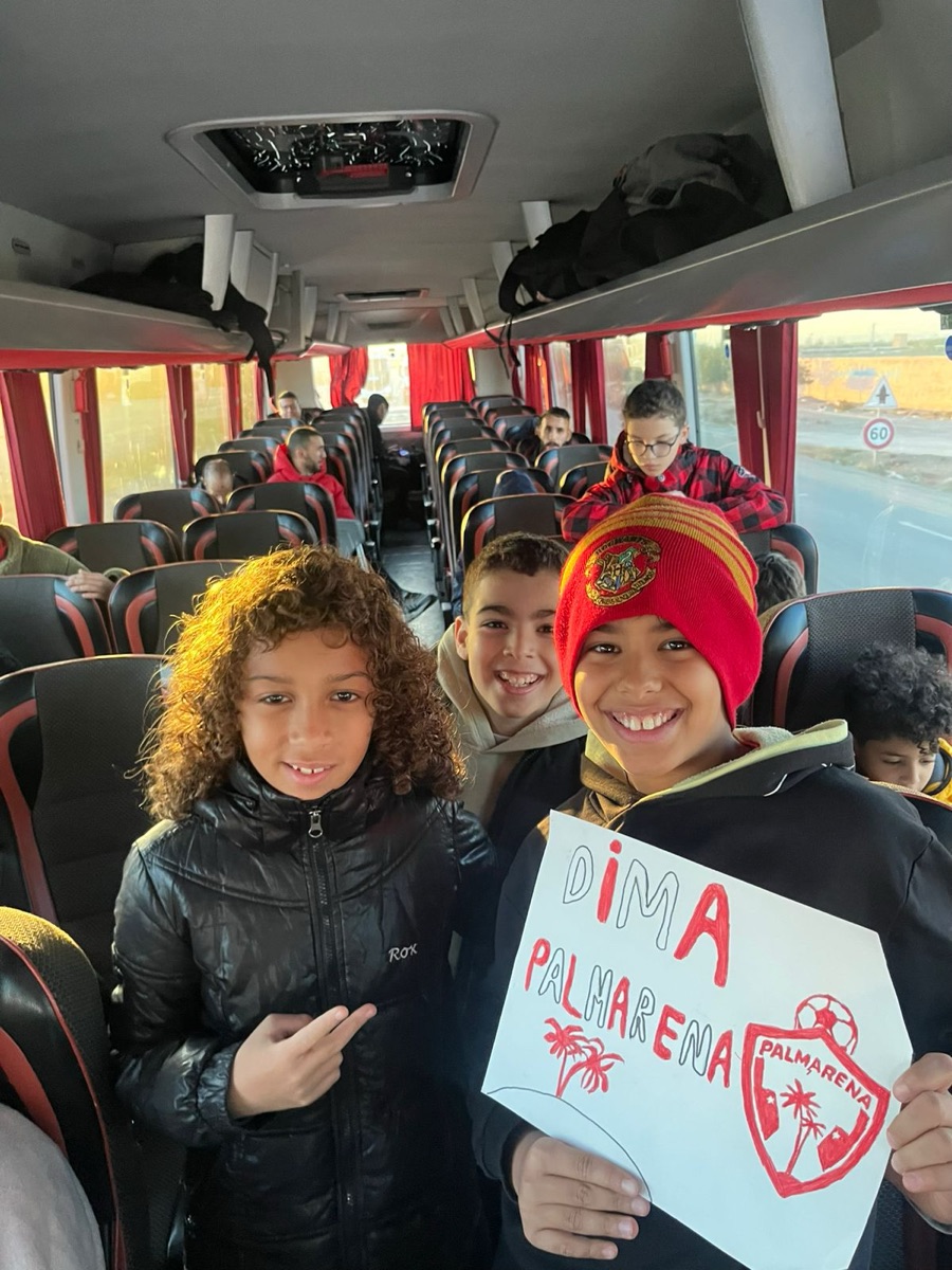 Trois jeunes joueurs dans le bus, pancarte « Dima Palmarena » à la main